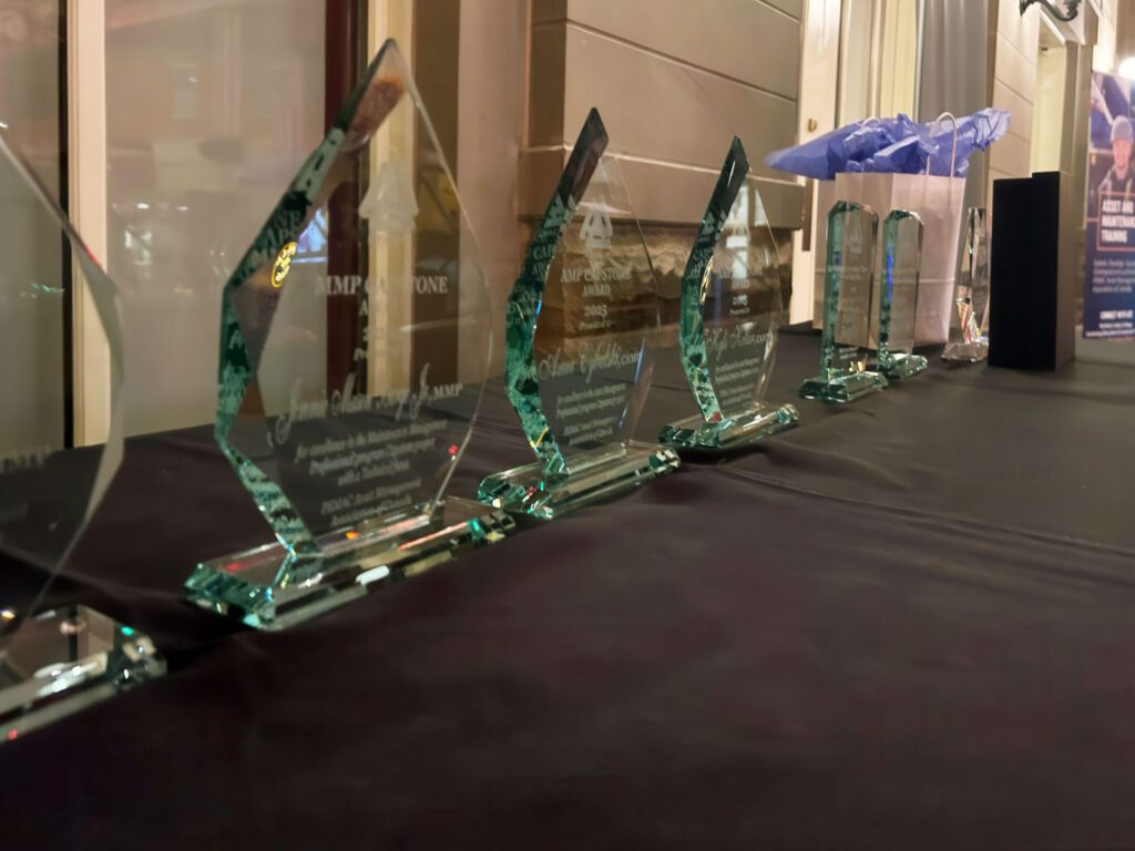Clear glass trophies displayed on a table, to be awarded to maintenance and reliability professionals.
