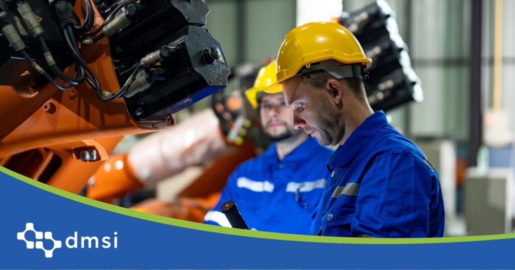 Two engineers check tablet data beside an orange industrial robotic arm on the plant floor.