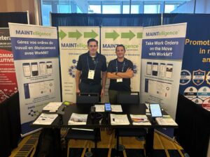John MacSween and Ilyass at the DMSI booth at MainTrain 2026 with MAINTelligence™ brochures, handheld devices and bilingual WorkMT bann