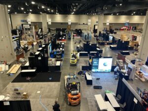 Exhibitors and forklifts setting up booths on the SMRP 2026 exhibit hall floor at the Raleigh Convention Center before the conference opens